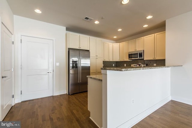 kitchen with dark wood-style flooring, visible vents, backsplash, stainless steel appliances, and dark stone counters