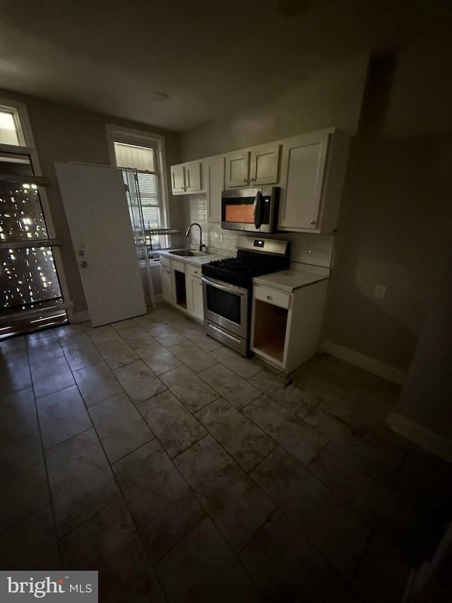 kitchen with a sink, stainless steel appliances, white cabinets, backsplash, and light countertops