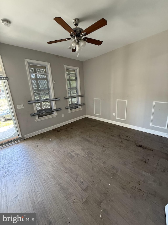 empty room featuring a ceiling fan, baseboards, and dark wood-style floors