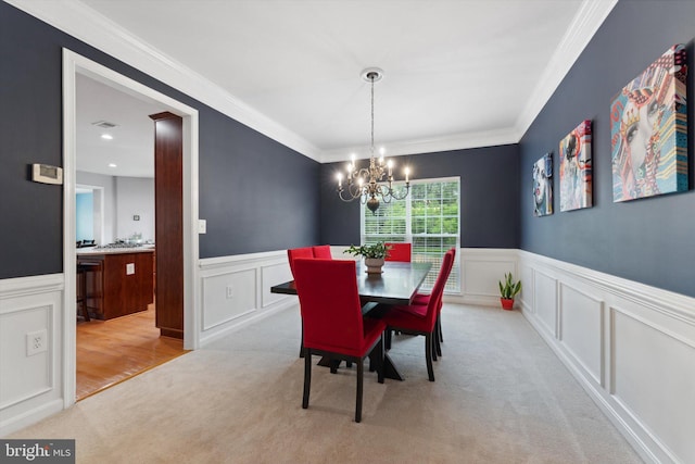 dining space with light colored carpet, wainscoting, a chandelier, and a decorative wall