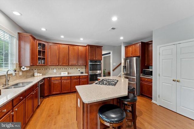 kitchen with a sink, stainless steel appliances, light wood-style flooring, a kitchen island, and a breakfast bar