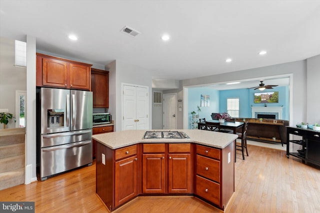 kitchen featuring stainless steel appliances, a kitchen island, a fireplace, light wood-type flooring, and a ceiling fan