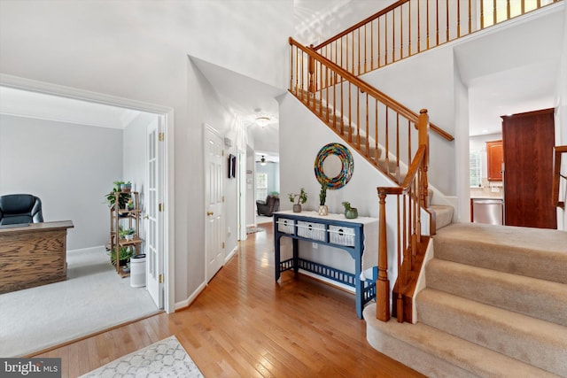 entrance foyer with light wood finished floors, a high ceiling, stairs, baseboards, and crown molding