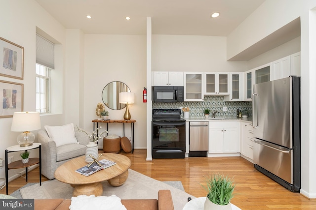 kitchen featuring glass insert cabinets, light wood-style flooring, white cabinetry, black appliances, and tasteful backsplash