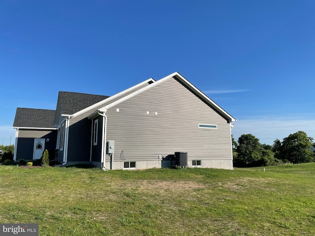 view of side of home featuring a shingled roof, a yard, and central AC