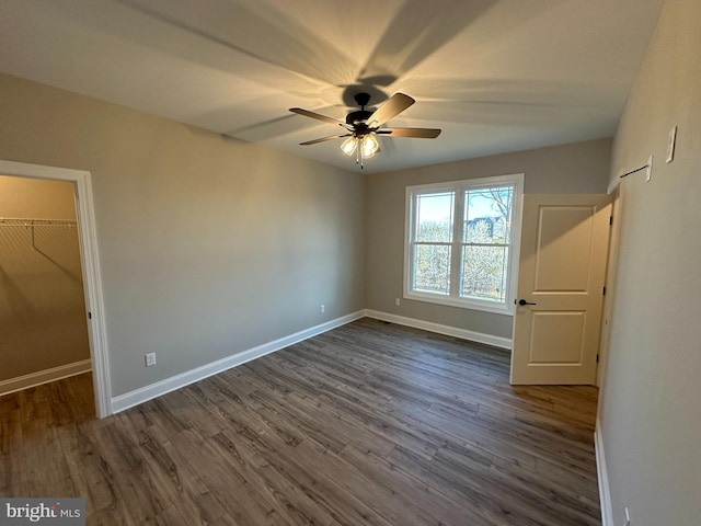 unfurnished bedroom featuring baseboards, a spacious closet, dark wood finished floors, and a closet