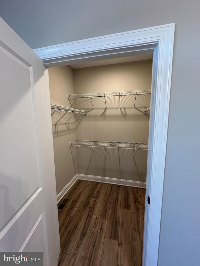 walk in closet with dark wood-style floors