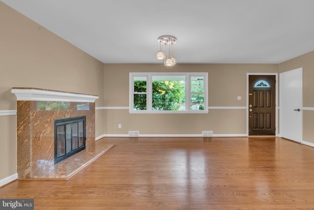 unfurnished living room featuring an inviting chandelier, visible vents, wood finished floors, and a high end fireplace