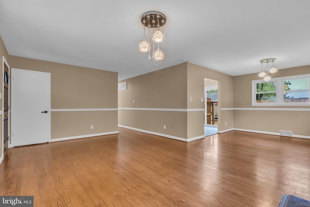 spare room featuring baseboards, a chandelier, visible vents, and wood finished floors