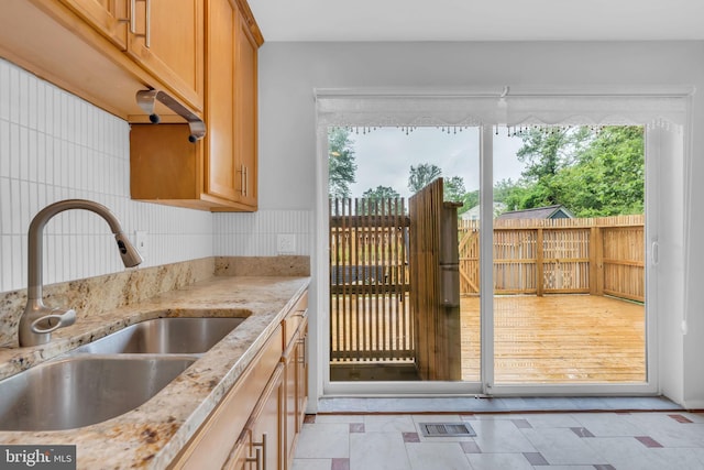kitchen featuring light stone countertops, tasteful backsplash, visible vents, and a sink