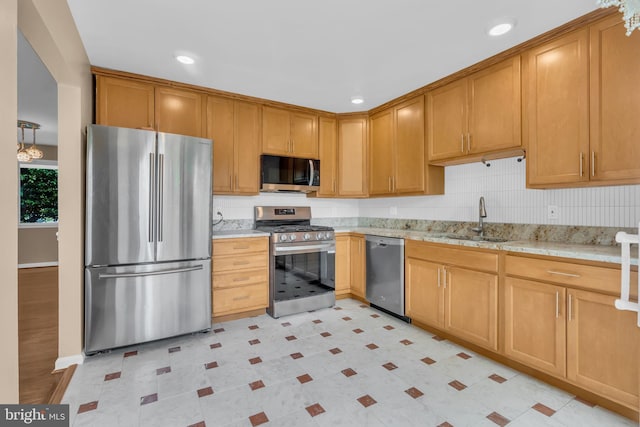 kitchen featuring baseboards, light stone counters, a sink, backsplash, and stainless steel appliances