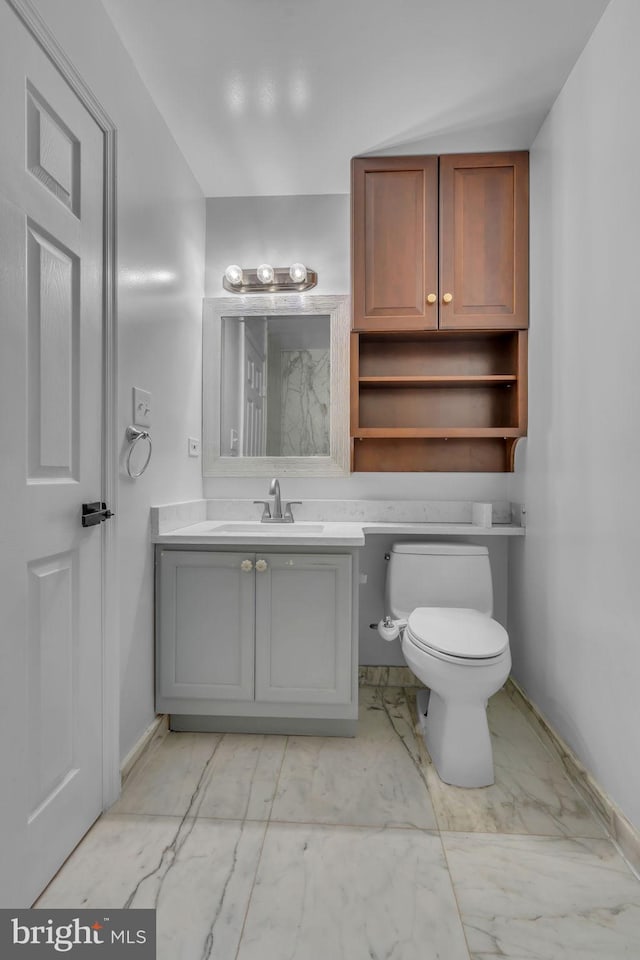 bathroom with toilet, marble finish floor, and baseboards