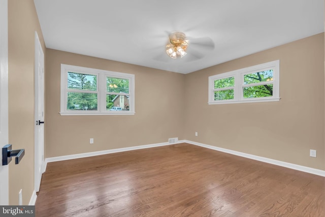 empty room featuring a ceiling fan, visible vents, wood finished floors, and baseboards
