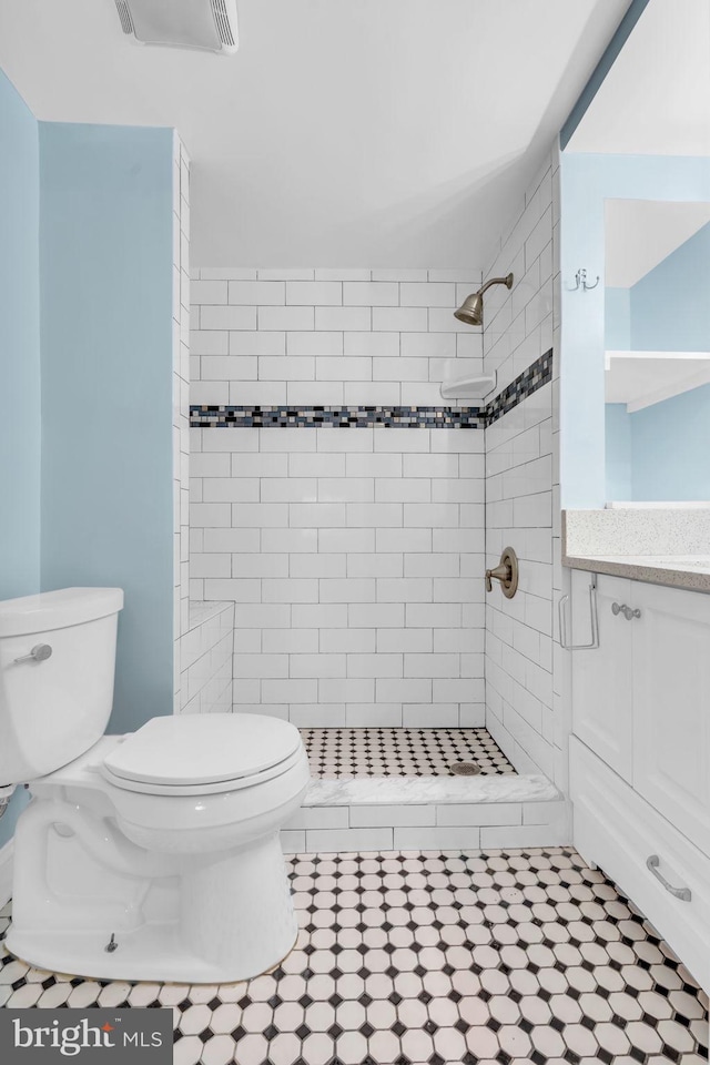 bathroom featuring toilet, vanity, visible vents, tile patterned flooring, and a tile shower