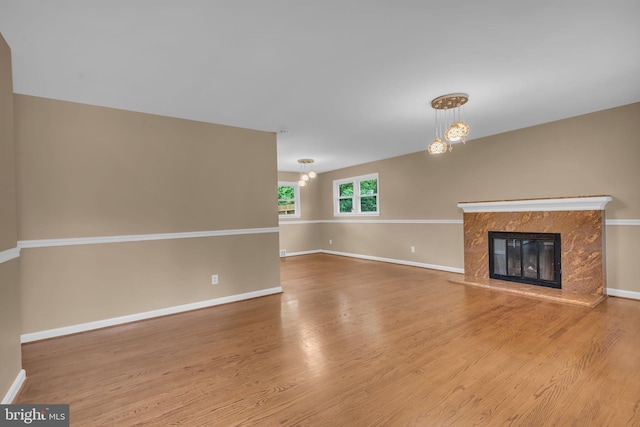 unfurnished living room with a premium fireplace, an inviting chandelier, baseboards, and wood finished floors