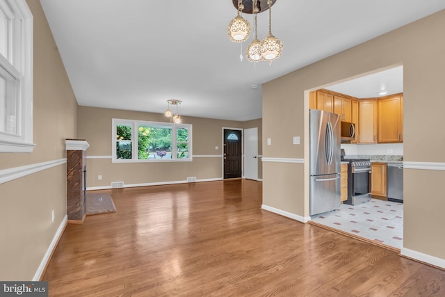 unfurnished living room featuring a notable chandelier, light wood-type flooring, baseboards, and visible vents