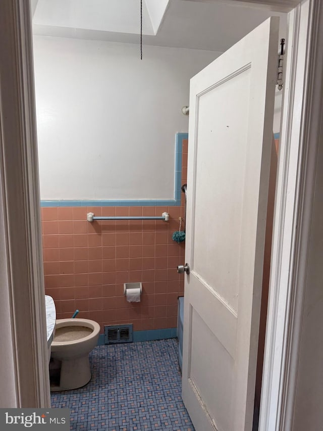 bathroom with toilet, tile patterned floors, tile walls, visible vents, and wainscoting