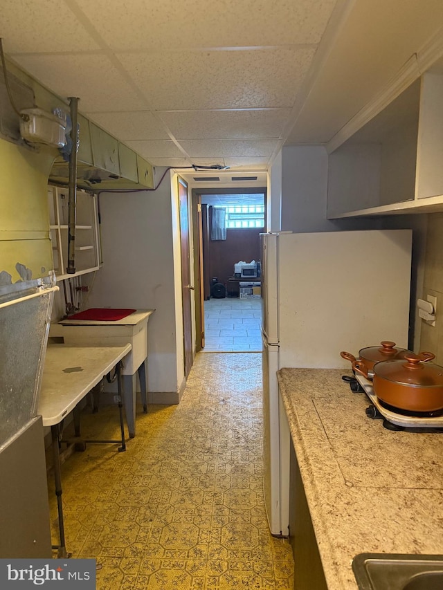 interior space with freestanding refrigerator, light floors, a drop ceiling, and light countertops