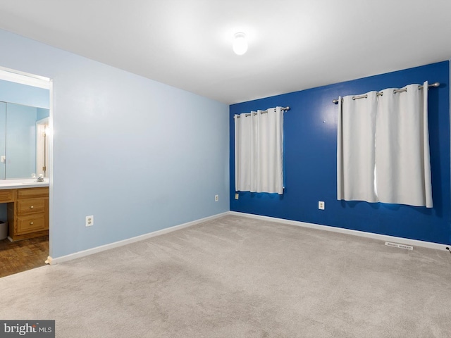 unfurnished bedroom with ensuite bath, carpet, baseboards, and visible vents