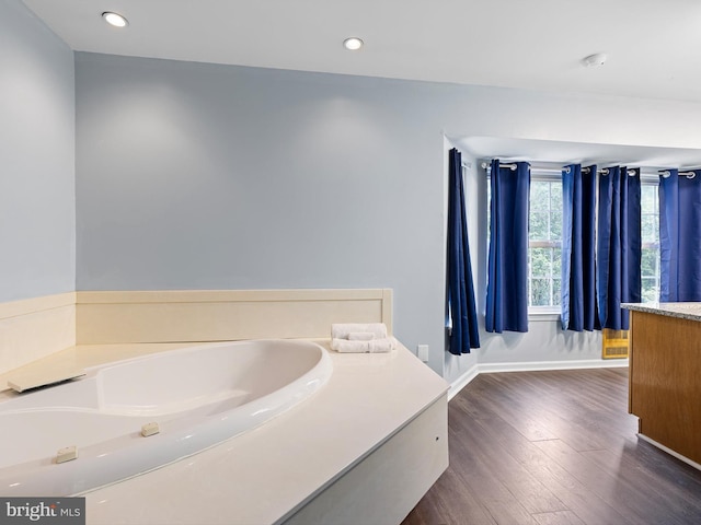 bathroom featuring wood finished floors, vanity, recessed lighting, baseboards, and a bath