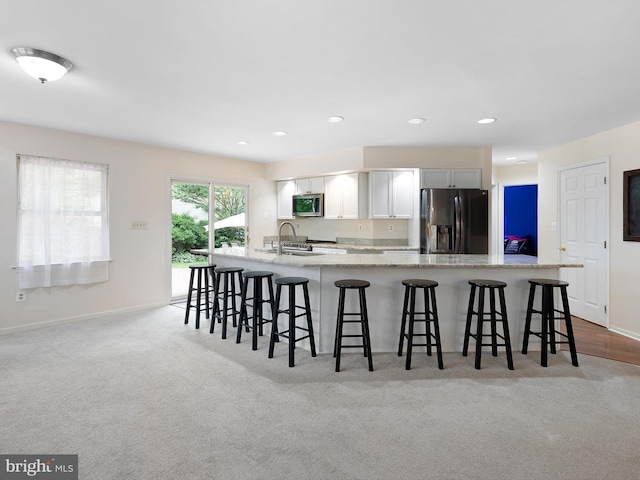 kitchen featuring a sink, a breakfast bar, stainless steel microwave, light carpet, and black refrigerator with ice dispenser