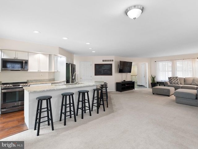 kitchen with stainless steel appliances, light colored carpet, a breakfast bar area, an island with sink, and white cabinetry