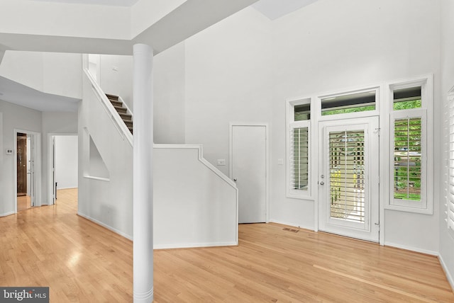 foyer with light wood finished floors, stairs, a high ceiling, and baseboards