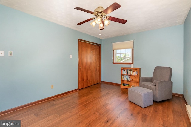 living area featuring baseboards, a ceiling fan, and wood finished floors