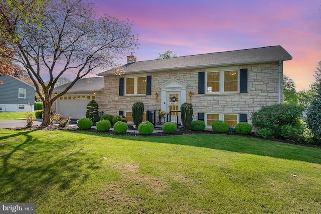 split foyer home with stone siding, a chimney, a lawn, and an attached garage