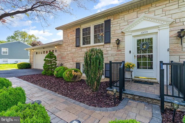 doorway to property featuring a garage, stone siding, and driveway