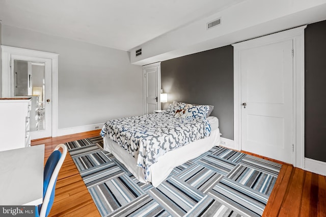 bedroom with baseboards, visible vents, and wood finished floors