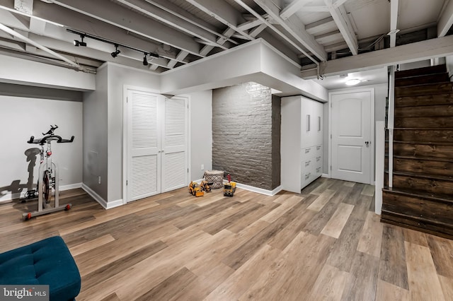 finished basement featuring rail lighting, stairway, light wood-type flooring, and baseboards