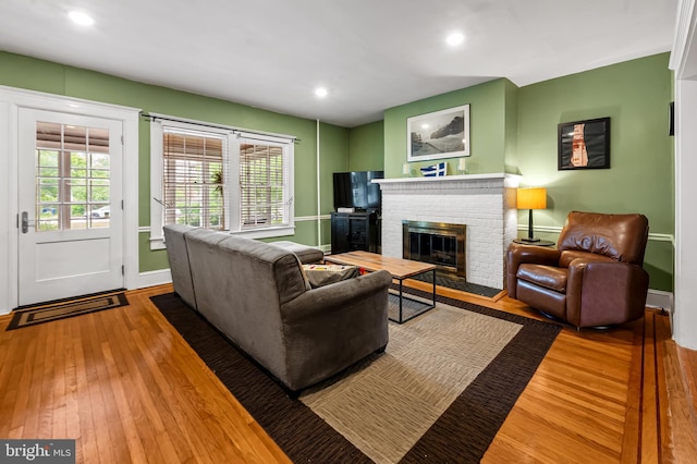 living room with a brick fireplace, baseboards, hardwood / wood-style floors, and a healthy amount of sunlight