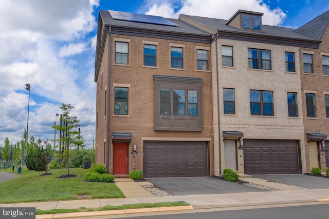 multi unit property with a garage, brick siding, solar panels, driveway, and a front yard
