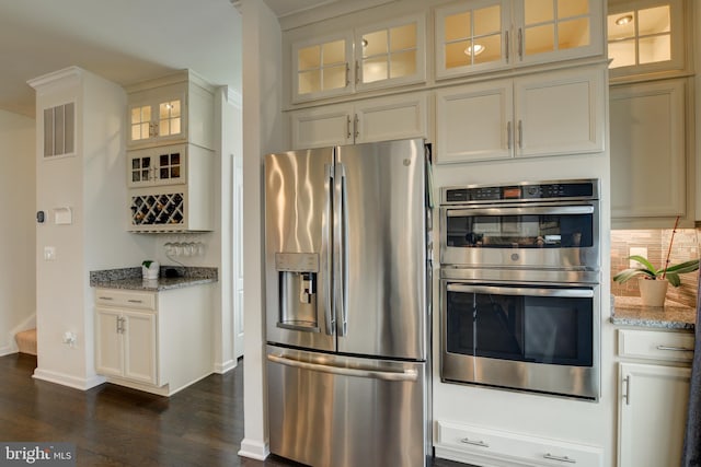kitchen with appliances with stainless steel finishes, dark wood-style floors, light stone counters, decorative backsplash, and baseboards