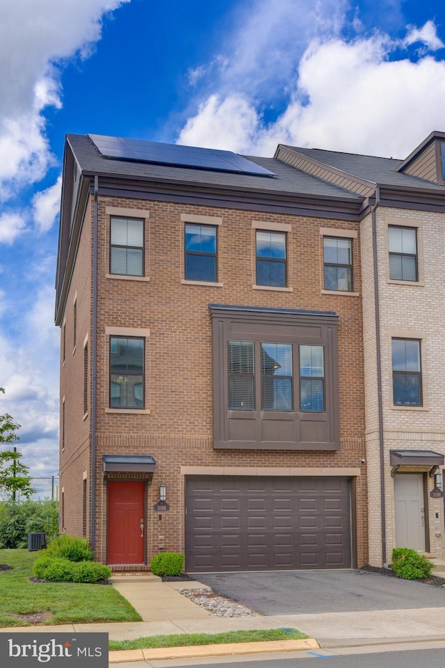 view of property with asphalt driveway, brick siding, roof mounted solar panels, a garage, and cooling unit