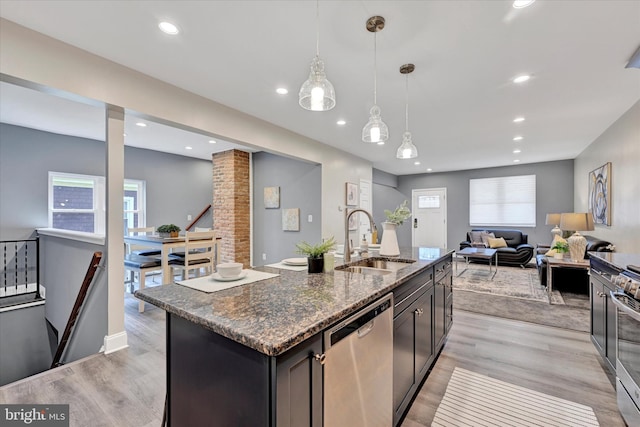kitchen featuring appliances with stainless steel finishes, a sink, light wood-style floors, dark stone countertops, and recessed lighting