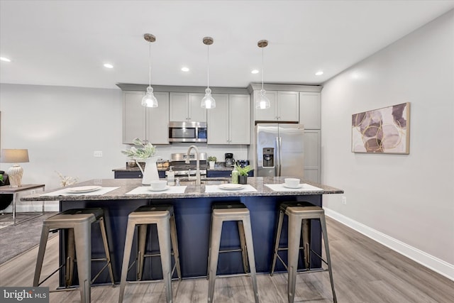 kitchen with stainless steel appliances, a sink, an island with sink, a breakfast bar, and light wood-style floors