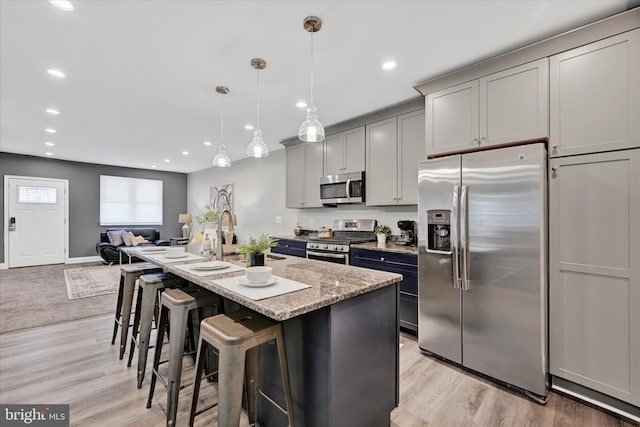 kitchen featuring appliances with stainless steel finishes, a sink, gray cabinetry, a breakfast bar area, and light stone counters