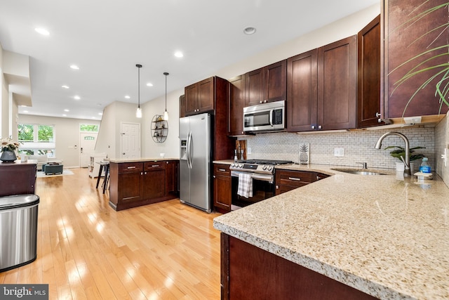 kitchen with a sink, tasteful backsplash, open floor plan, hanging light fixtures, and appliances with stainless steel finishes
