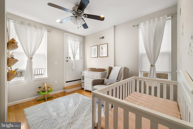 bedroom featuring baseboards, light wood-style floors, ceiling fan, and a crib