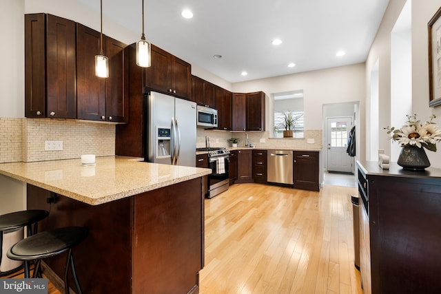 kitchen with a peninsula, stainless steel appliances, a kitchen breakfast bar, decorative light fixtures, and backsplash