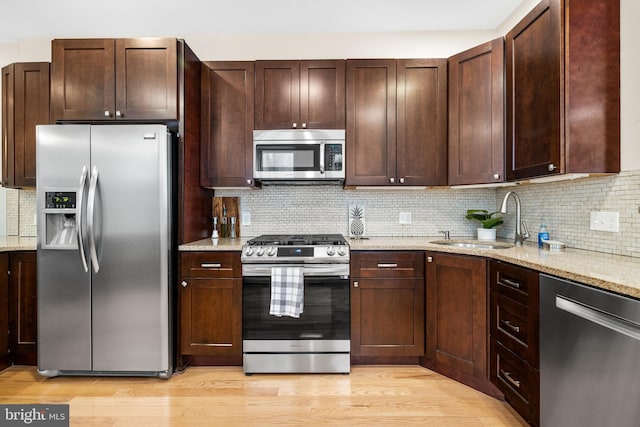 kitchen with appliances with stainless steel finishes, decorative backsplash, light stone countertops, and a sink