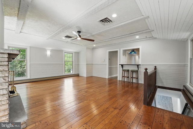 unfurnished living room featuring a wainscoted wall, visible vents, a ceiling fan, and wood-type flooring