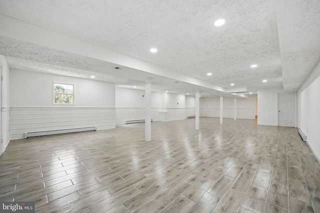 below grade area featuring a textured ceiling, wood finished floors, wainscoting, and a baseboard heating unit