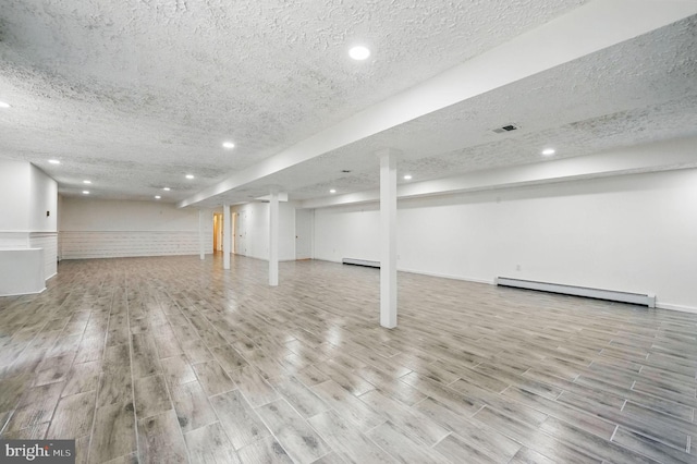 finished below grade area with visible vents, a baseboard radiator, and recessed lighting
