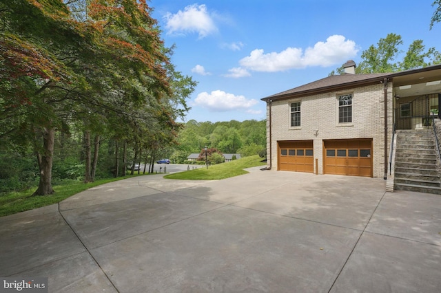 view of side of home featuring an attached garage, brick siding, driveway, stairway, and a chimney