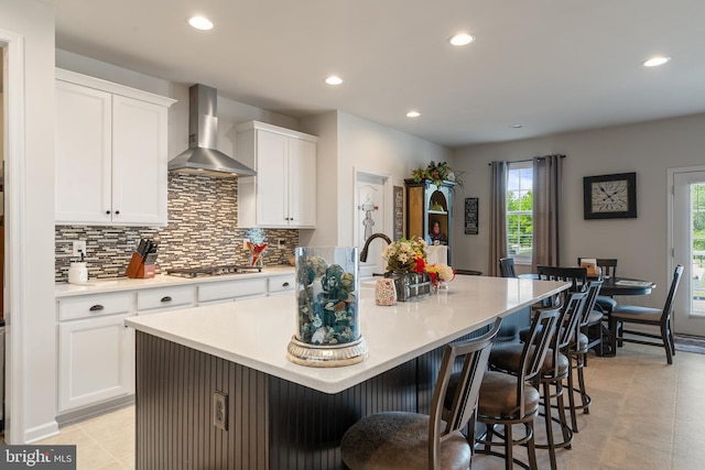 kitchen with wall chimney exhaust hood, stainless steel gas stovetop, recessed lighting, tasteful backsplash, and a kitchen island with sink
