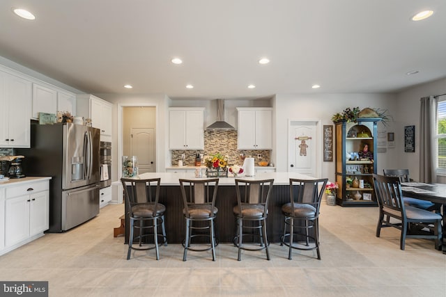 kitchen featuring wall chimney range hood, stainless steel fridge, decorative backsplash, a center island, and white cabinets