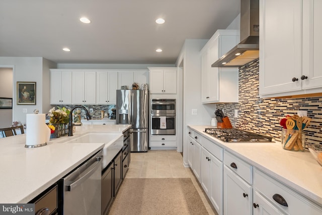 kitchen featuring wall chimney exhaust hood, stainless steel appliances, a sink, white cabinetry, and light countertops